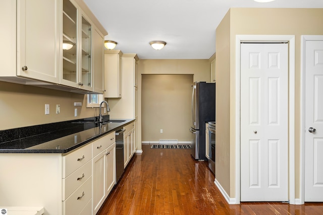 kitchen with stainless steel appliances, dark wood-type flooring, a sink, baseboards, and glass insert cabinets