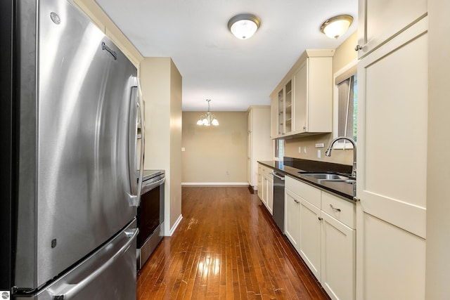 kitchen featuring dark countertops, dark wood-style floors, glass insert cabinets, stainless steel appliances, and a sink