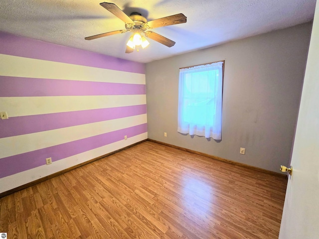 spare room with ceiling fan, a textured ceiling, baseboards, and wood finished floors