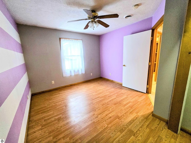 unfurnished bedroom featuring a textured ceiling, wood finished floors, a ceiling fan, visible vents, and baseboards