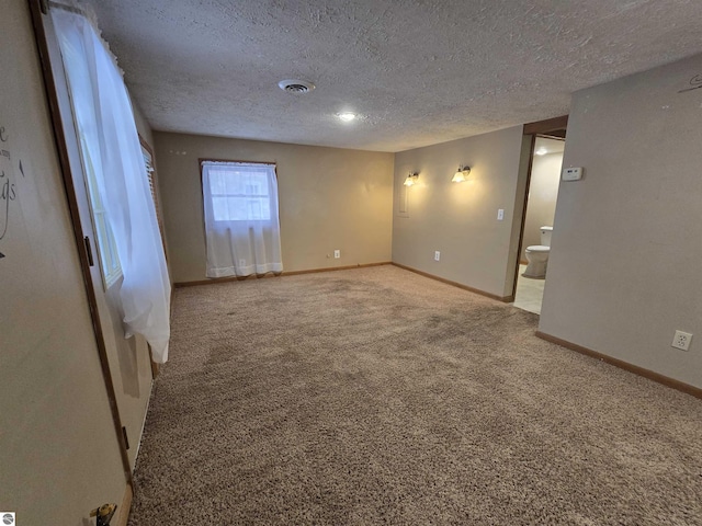 spare room with carpet floors, visible vents, a textured ceiling, and baseboards