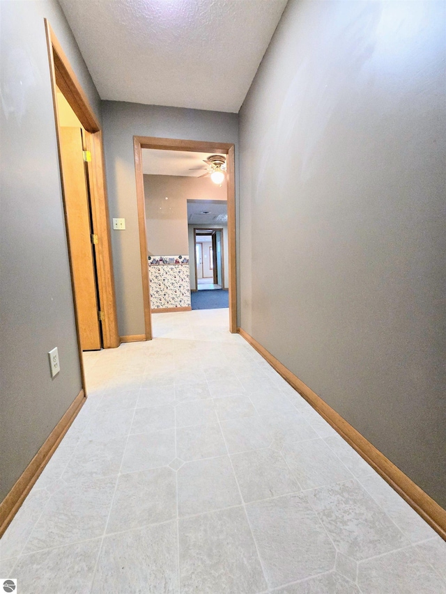 corridor featuring a textured ceiling, baseboards, and light tile patterned floors