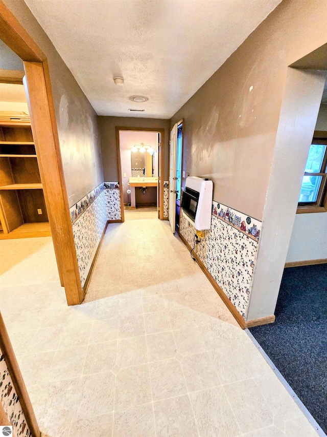 hall featuring heating unit, a wainscoted wall, and a textured ceiling