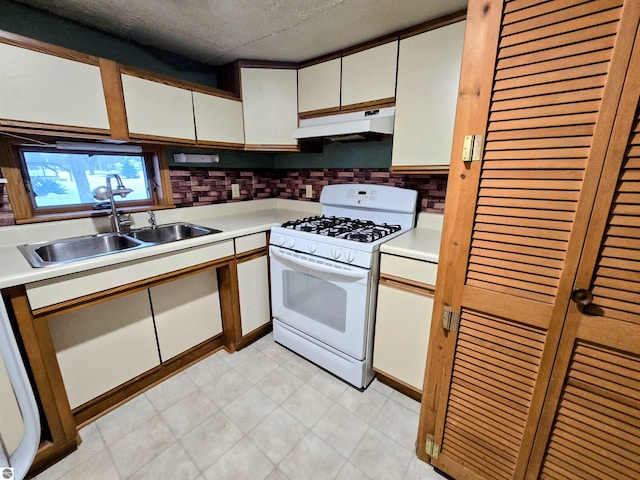 kitchen with light countertops, white gas stove, under cabinet range hood, white cabinetry, and a sink