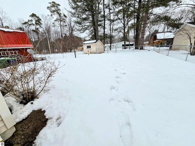 yard layered in snow with a storage unit, fence, and an outbuilding