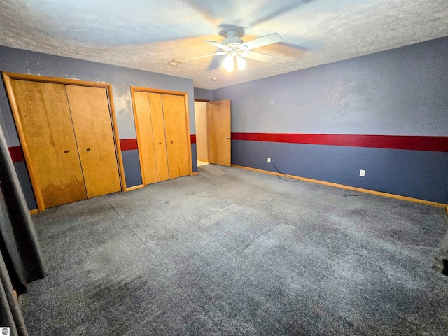 unfurnished bedroom featuring a ceiling fan, a textured ceiling, baseboards, and two closets