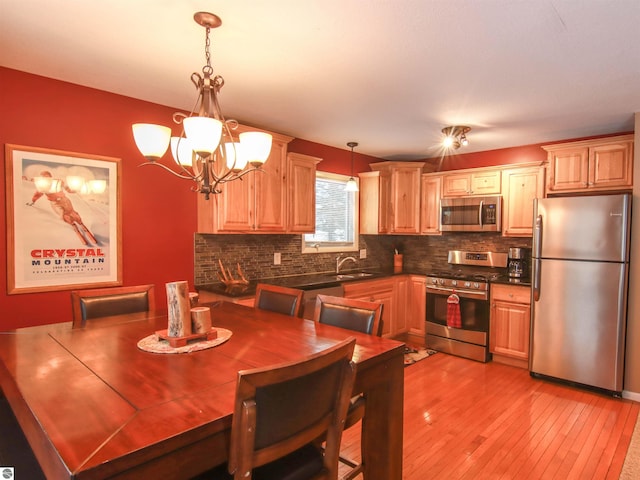 kitchen featuring light wood finished floors, tasteful backsplash, dark countertops, decorative light fixtures, and stainless steel appliances