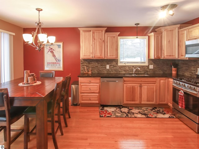 kitchen featuring light wood-style flooring, stainless steel appliances, a sink, decorative backsplash, and dark countertops