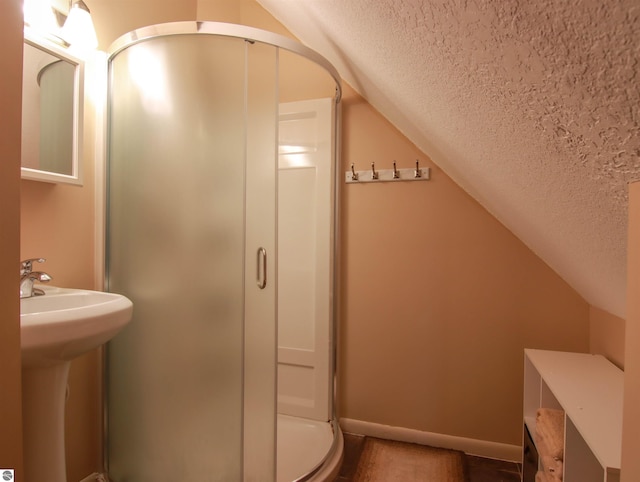 bathroom featuring a sink, vaulted ceiling, a textured ceiling, a shower stall, and baseboards