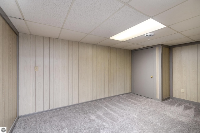 finished basement featuring wooden walls, visible vents, a drop ceiling, and carpet flooring