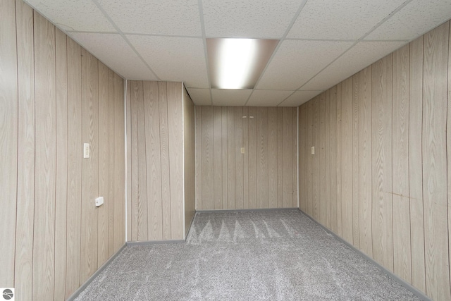 carpeted empty room with wooden walls and a drop ceiling