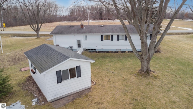 rear view of house with roof with shingles, a chimney, and a yard