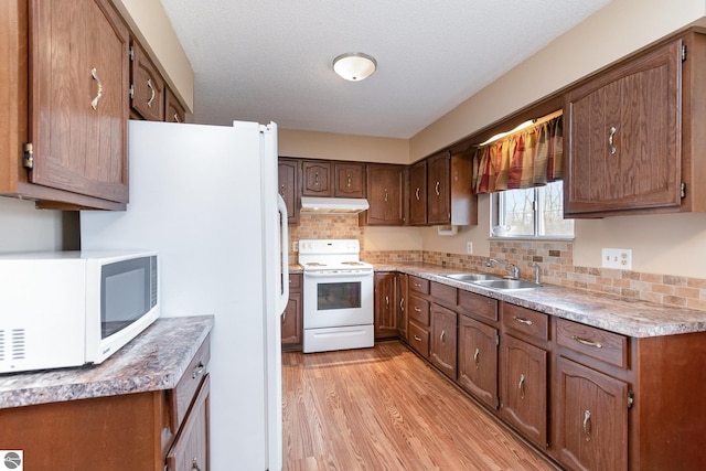 kitchen featuring backsplash, light wood-style floors, a sink, white appliances, and under cabinet range hood