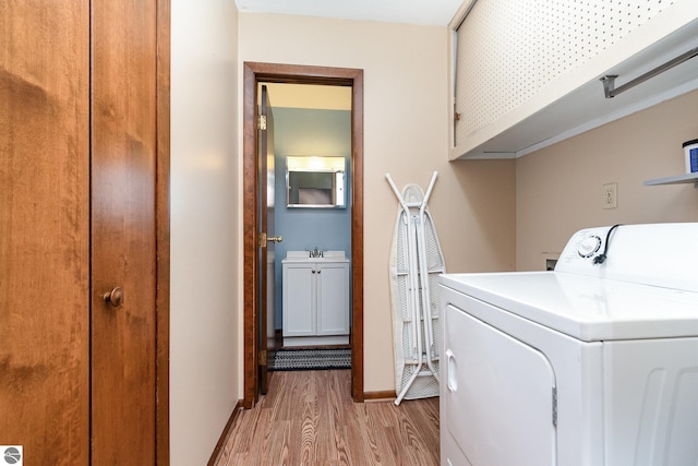 clothes washing area with cabinet space, baseboards, washer / clothes dryer, light wood-type flooring, and a sink