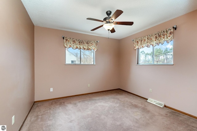 unfurnished room featuring a ceiling fan, light colored carpet, visible vents, and baseboards