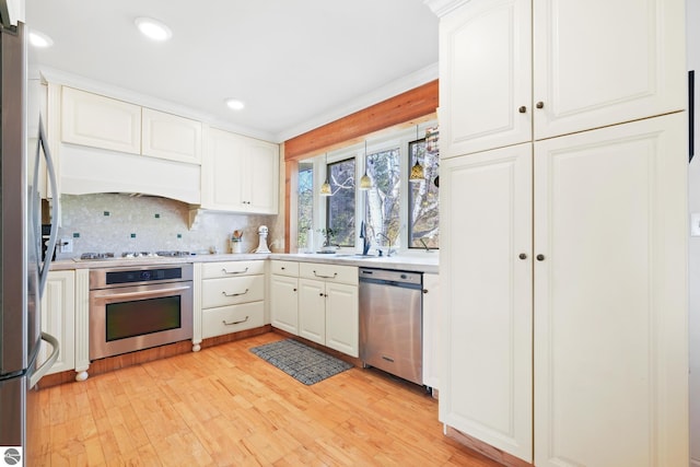 kitchen with stainless steel appliances, white cabinets, light countertops, light wood finished floors, and tasteful backsplash