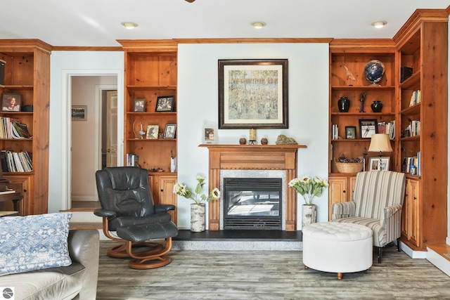 living area with ornamental molding, wood finished floors, a glass covered fireplace, and built in shelves