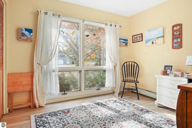 sitting room with a baseboard heating unit, wood finished floors, and baseboards