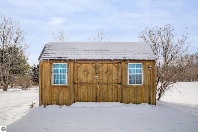 snow covered structure featuring a storage shed and an outbuilding