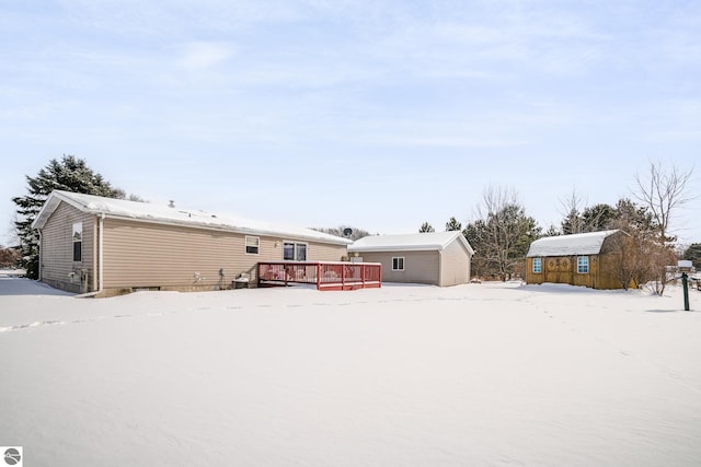 snow covered house with an outdoor structure and a deck