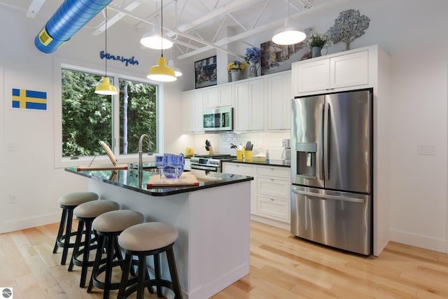 kitchen featuring white cabinets, decorative backsplash, dark countertops, stainless steel appliances, and light wood-style floors