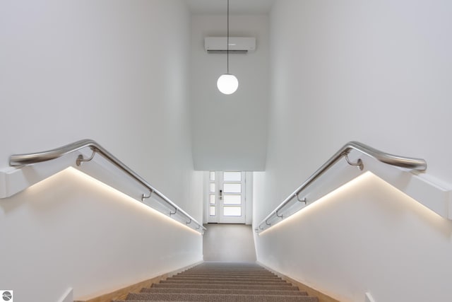 staircase with an AC wall unit and a towering ceiling