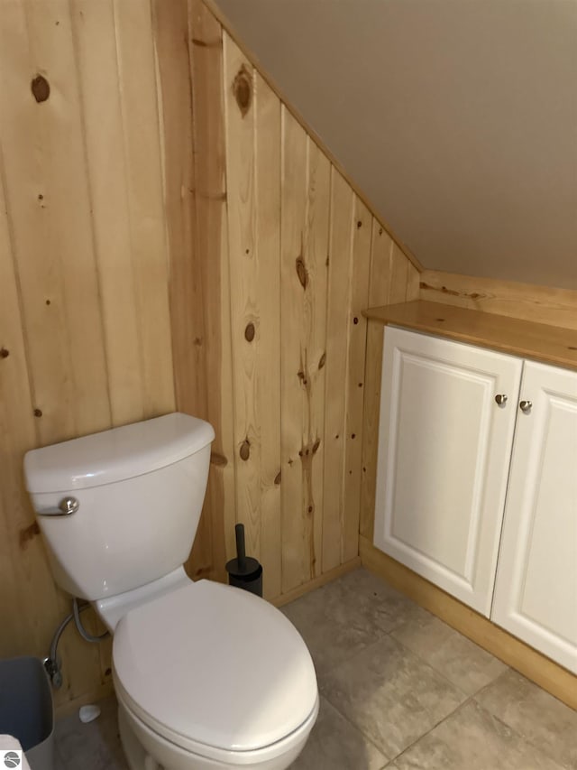 bathroom with toilet, wood walls, and tile patterned floors