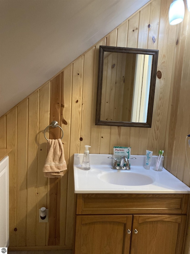 bathroom featuring vaulted ceiling, wooden walls, and vanity