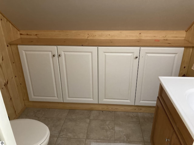 bathroom with toilet, tile patterned flooring, wooden walls, and vanity