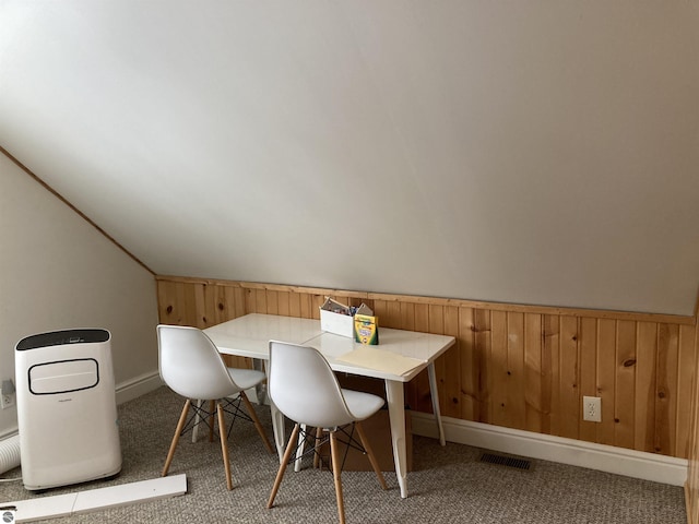 unfurnished dining area featuring carpet floors, a wainscoted wall, lofted ceiling, visible vents, and wood walls