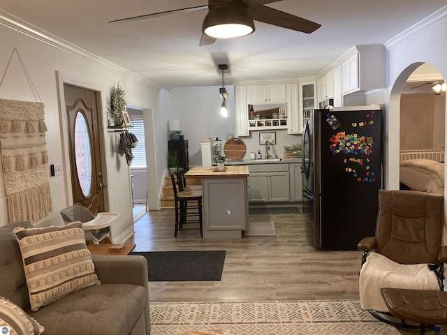 living room with light wood-type flooring, arched walkways, crown molding, and ceiling fan