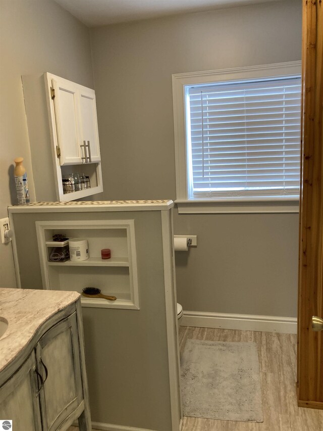 half bathroom with baseboards, vanity, toilet, and wood finished floors