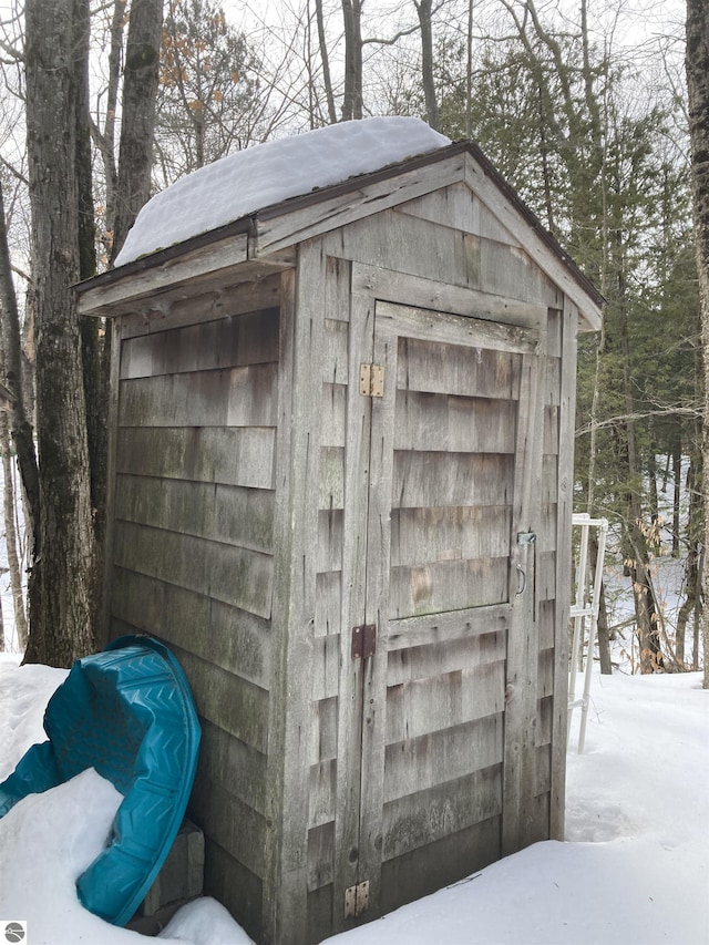 snow covered structure with a storage shed and an outbuilding