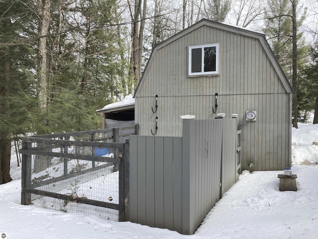 snow covered property featuring a gate, fence, and a gambrel roof