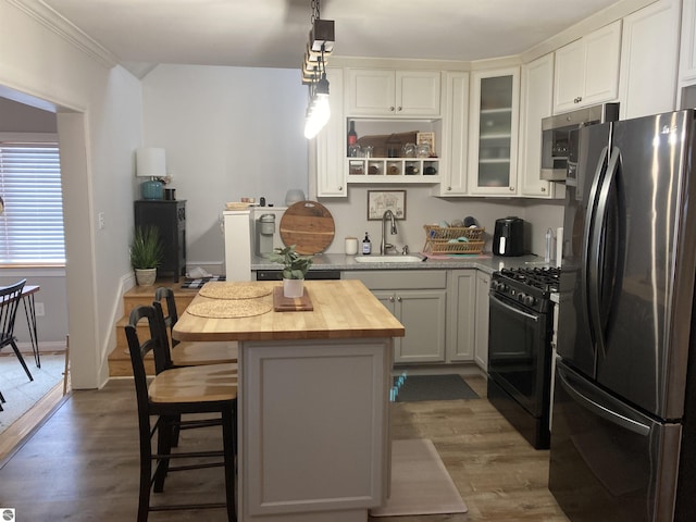 kitchen featuring a center island, wooden counters, black gas range oven, freestanding refrigerator, and a sink