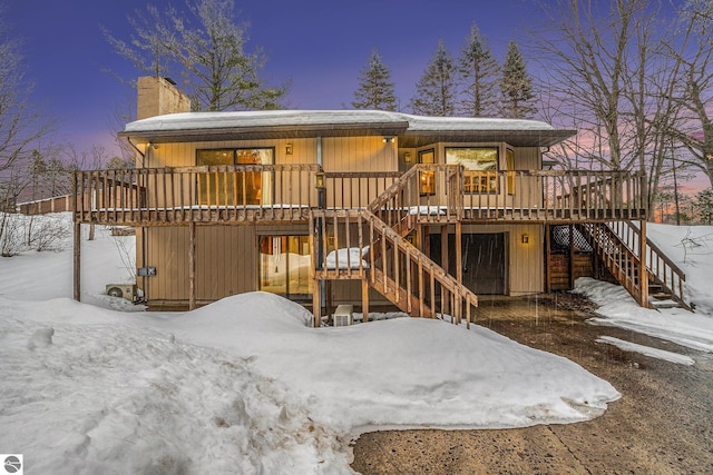 snow covered property featuring a deck, stairway, and a chimney