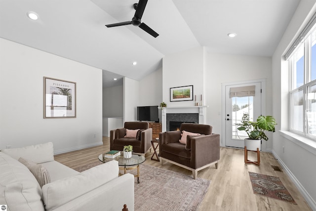 living area with visible vents, baseboards, lofted ceiling, a lit fireplace, and light wood-type flooring