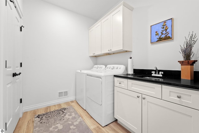 clothes washing area featuring cabinet space, visible vents, light wood-style floors, a sink, and washer and dryer