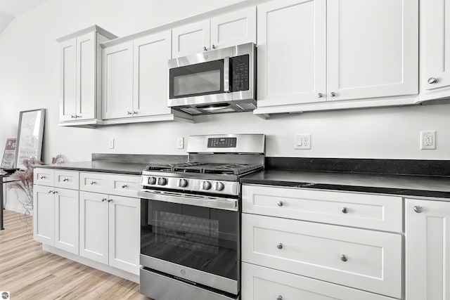 kitchen with appliances with stainless steel finishes, dark countertops, light wood-type flooring, and white cabinetry