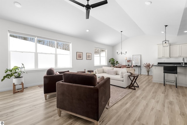 living room with lofted ceiling, light wood-style floors, baseboards, and ceiling fan with notable chandelier