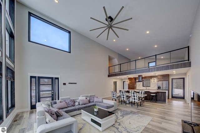 living area featuring light wood finished floors, baseboards, ceiling fan, recessed lighting, and a towering ceiling