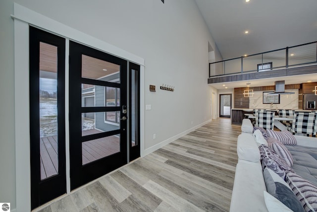 living area with recessed lighting, baseboards, light wood-type flooring, and a towering ceiling