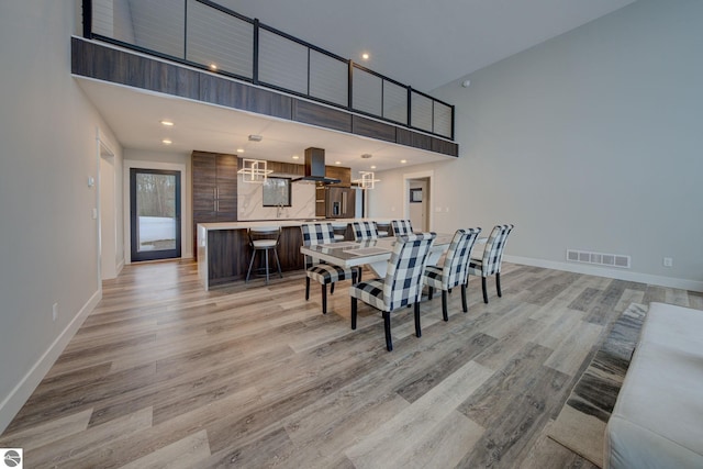 dining room with visible vents, recessed lighting, light wood finished floors, baseboards, and a towering ceiling