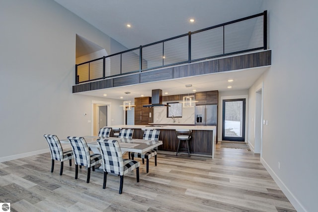 dining room with a towering ceiling, recessed lighting, baseboards, and light wood finished floors