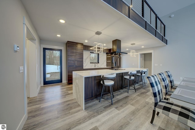 kitchen featuring light countertops, a kitchen breakfast bar, modern cabinets, light wood-type flooring, and island range hood