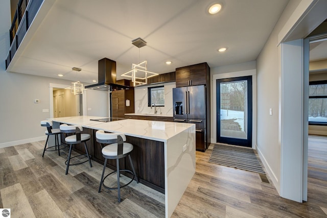 kitchen with modern cabinets, high end fridge, island exhaust hood, dark brown cabinetry, and black electric stovetop