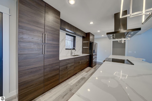 kitchen featuring light stone countertops, light wood-type flooring, island range hood, modern cabinets, and a sink