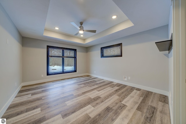 spare room with a tray ceiling, baseboards, and light wood-style floors