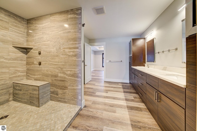 bathroom featuring visible vents, a sink, wood finished floors, double vanity, and tiled shower