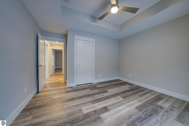 unfurnished bedroom featuring a tray ceiling and wood finished floors